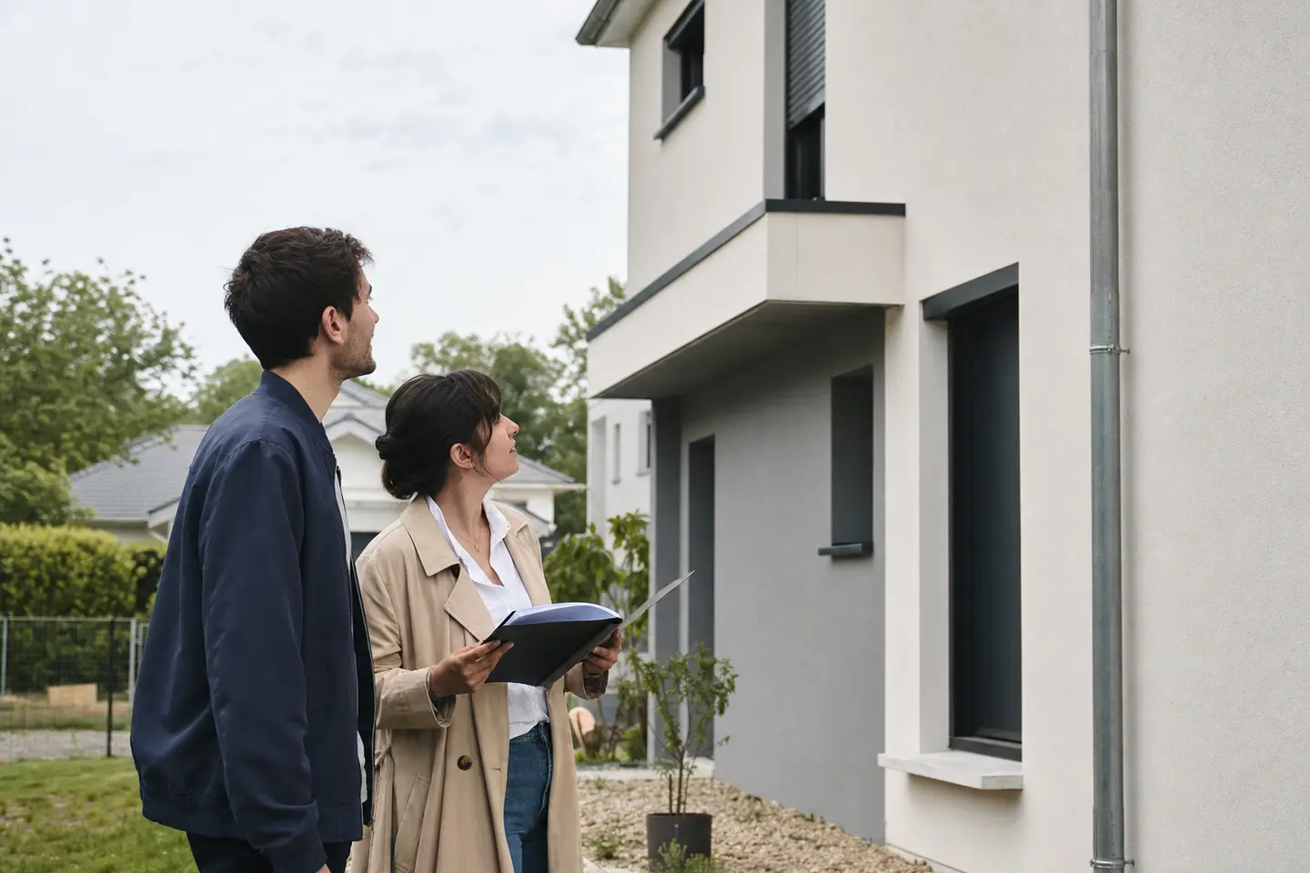 Couple d'acquéreurs inspectant la façade d'une maison récente lors d'une visite avant achat