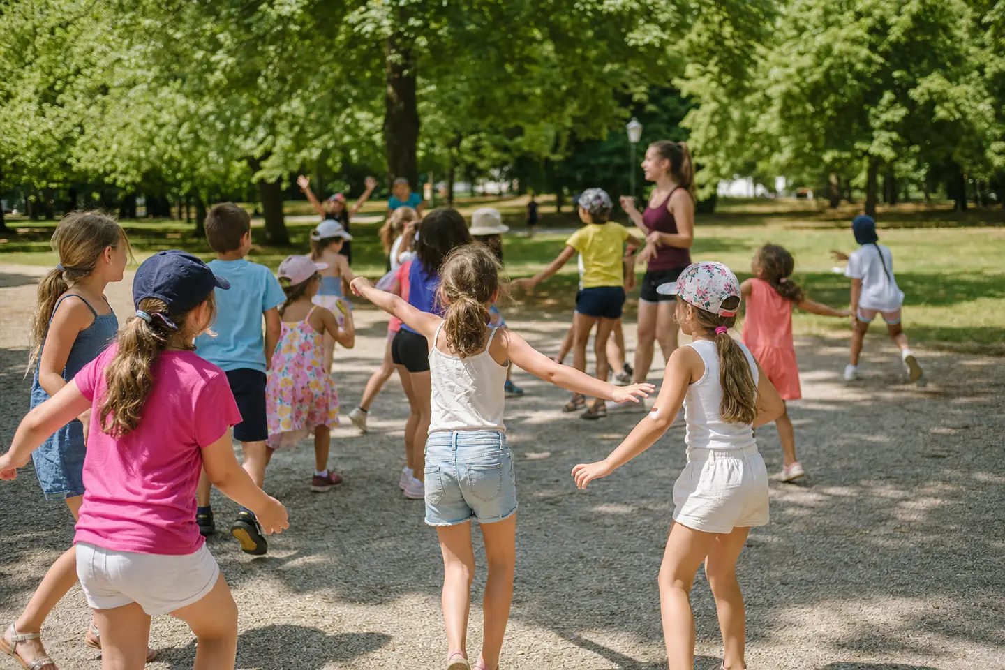Groupe d'enfants jouant en plein air dans un parc lors d'un accueil de loisirs d'été en France, un animateur veillant en arrière-plan