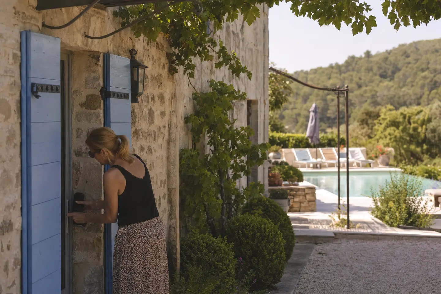 Maison de vacances en pierre avec volets bleus, l'hôte installe une boîte à clés avant l'arrivée des locataires