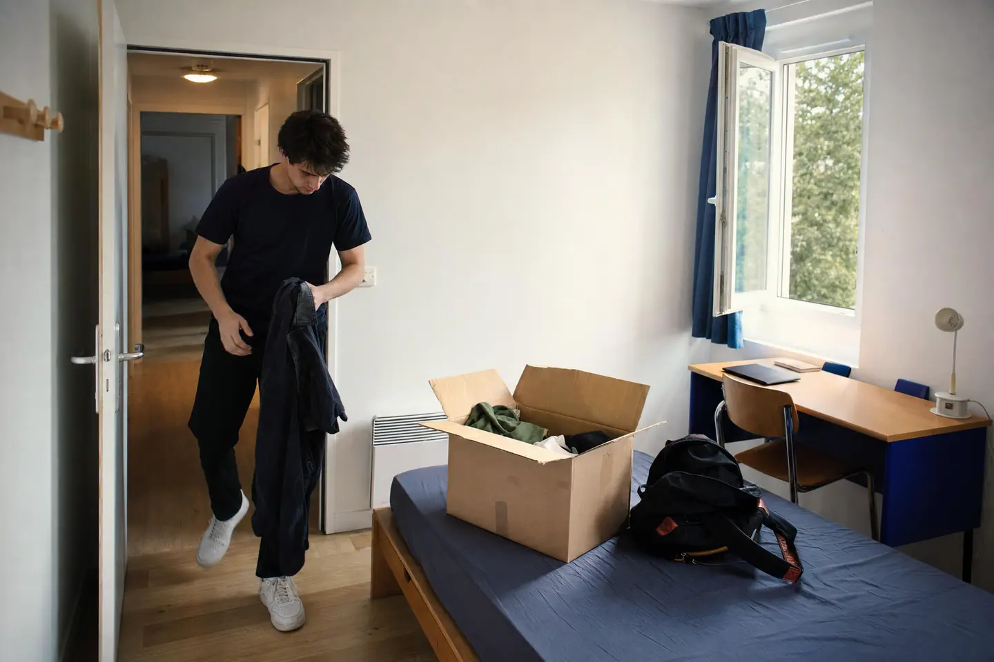 Étudiant emménageant dans une chambre de résidence universitaire CROUS, carton posé sur le lit