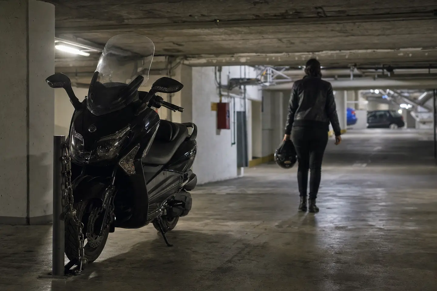 Maxi-scooter attaché à un point fixe avec une chaîne antivol dans un parking souterrain