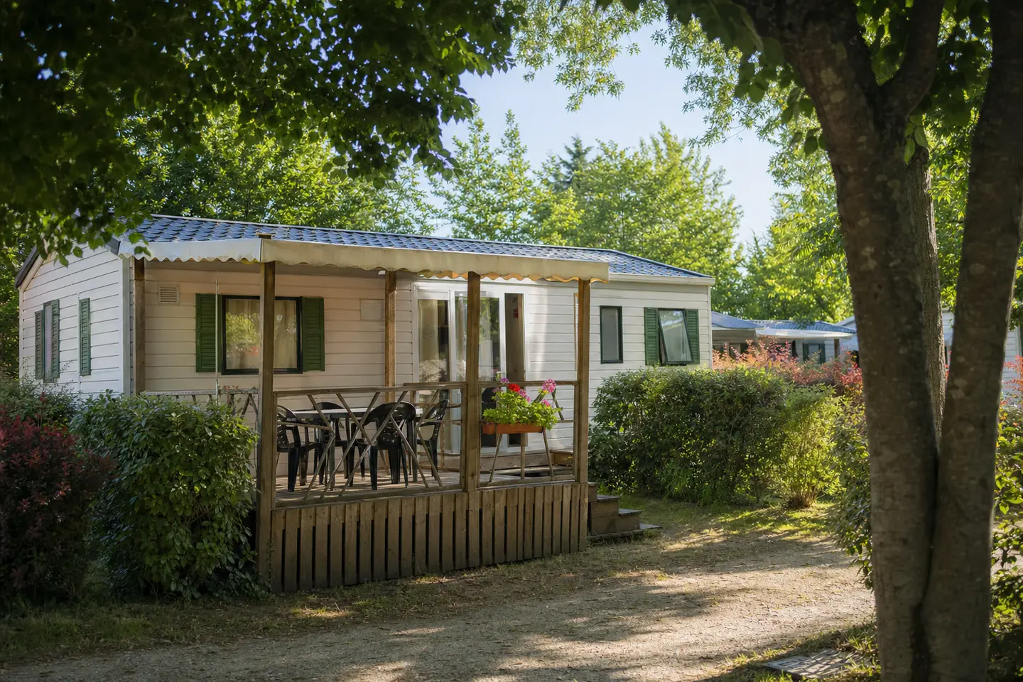 Mobil-home entretenu avec terrasse en bois sur une parcelle arborée de camping en France, au petit matin
