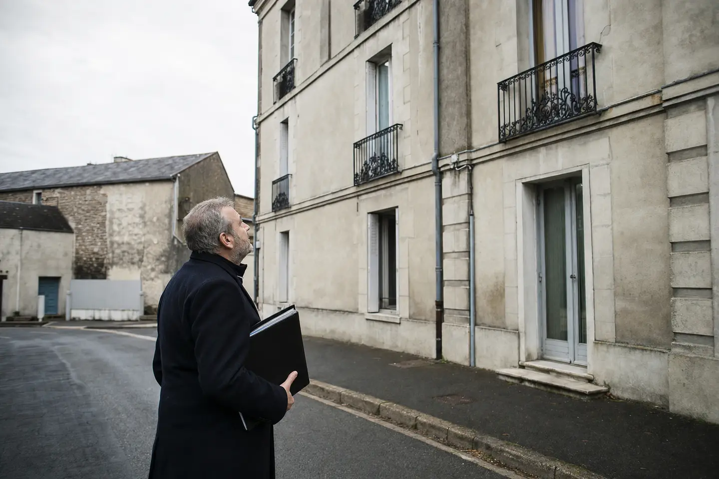 Propriétaire bailleur devant son immeuble en copropriété, dossier d'assurance sous le bras