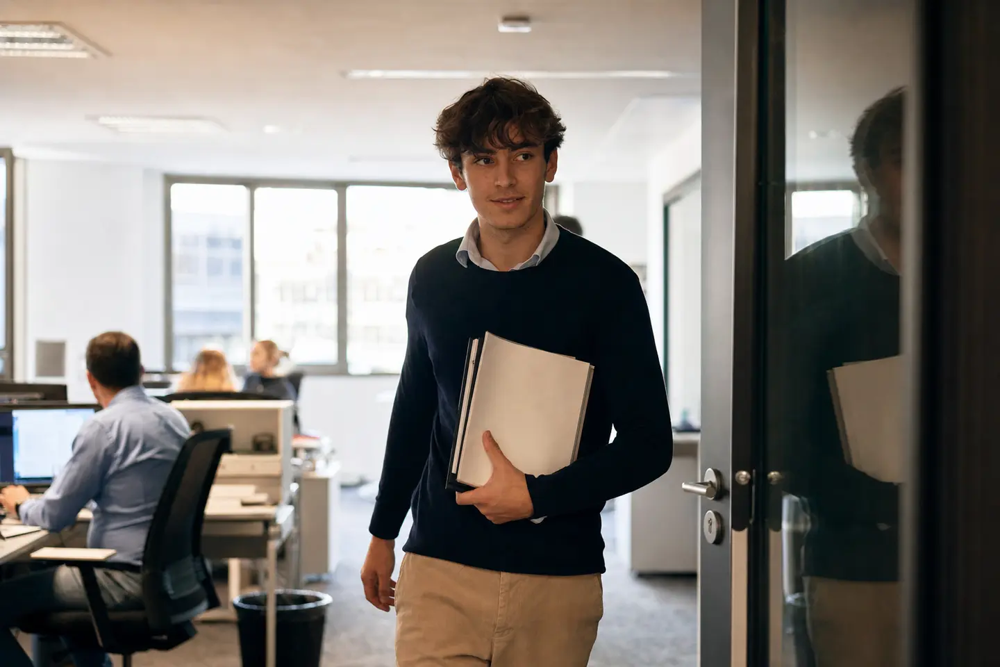 Jeune stagiaire entrant dans des bureaux modernes son premier jour, dossier de convention de stage à la main