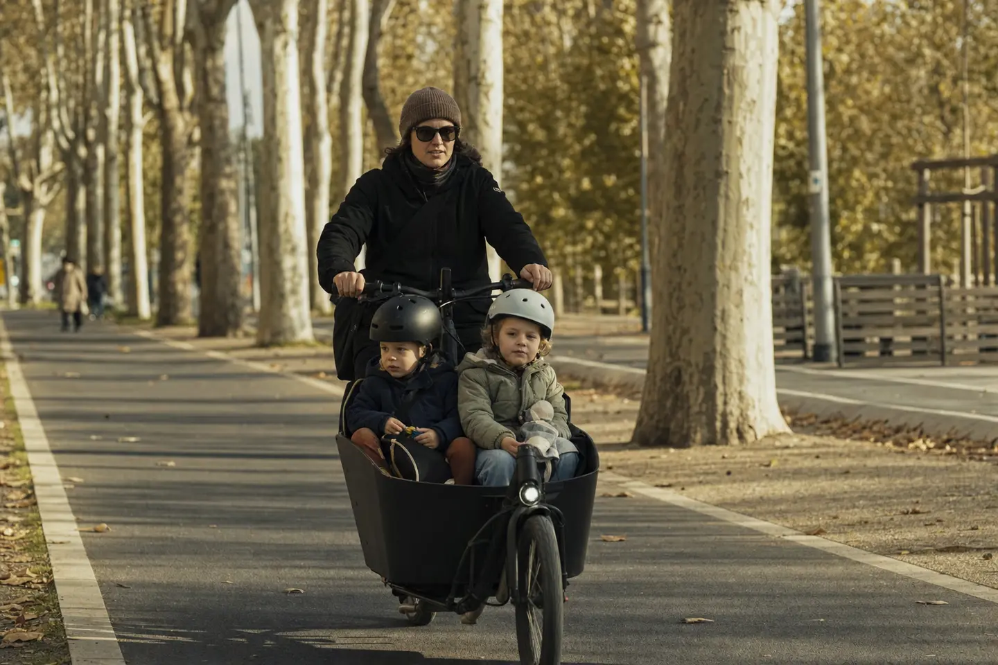 Parent transportant deux enfants dans la caisse d'un vélo cargo électrique sur une piste cyclable en ville