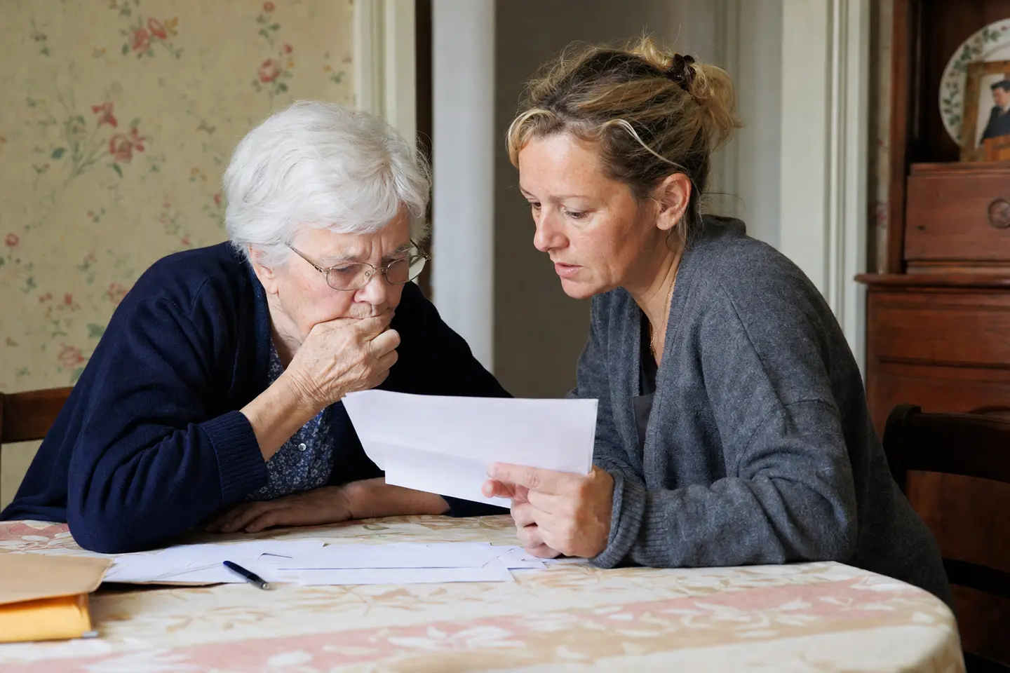 Une femme aide sa mère âgée à relire un courrier administratif à la table de la salle à manger