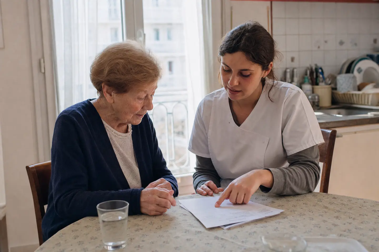 Une aide à domicile et une personne âgée examinent ensemble un dossier d'allocation autour d'une table