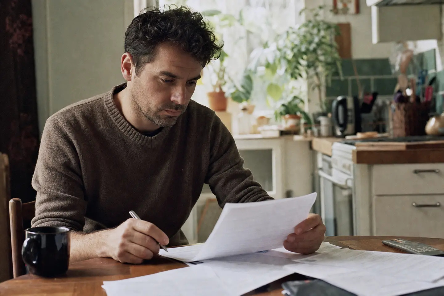 Un emprunteur relit attentivement les clauses d'exclusion de son contrat d'assurance de prêt à la table de sa cuisine