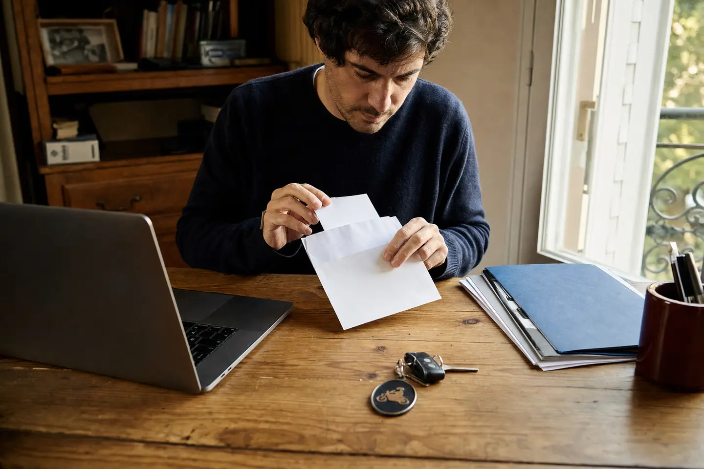 Personne glissant une lettre de résiliation dans une enveloppe, clés de moto et contrat d'assurance posés sur le bureau