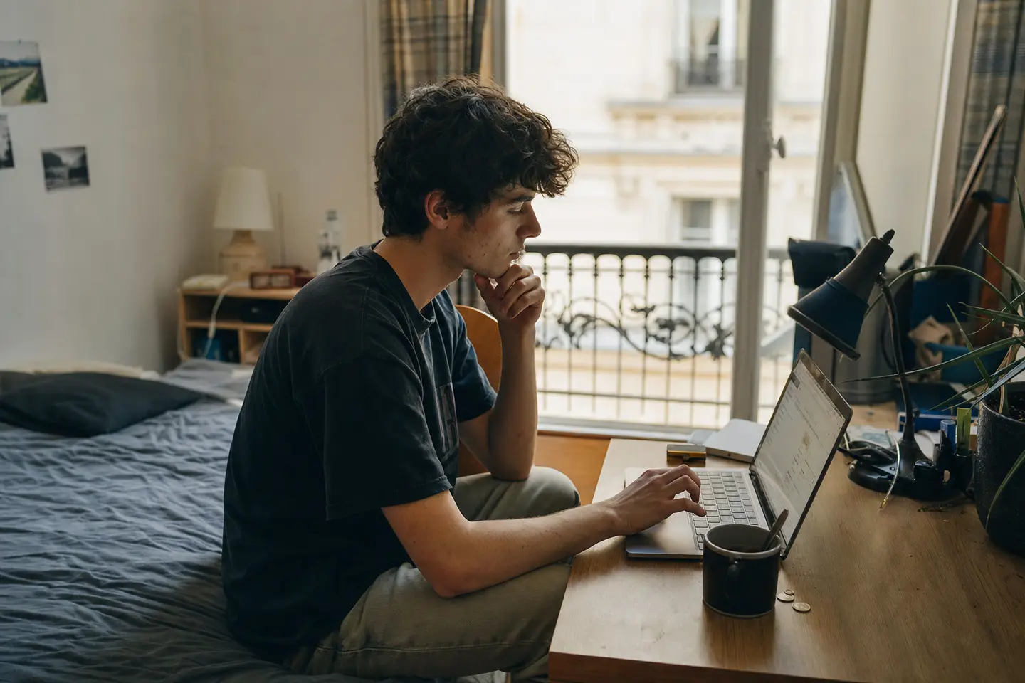 Étudiant comparant des devis de mutuelle sur son ordinateur portable dans une petite chambre étudiante