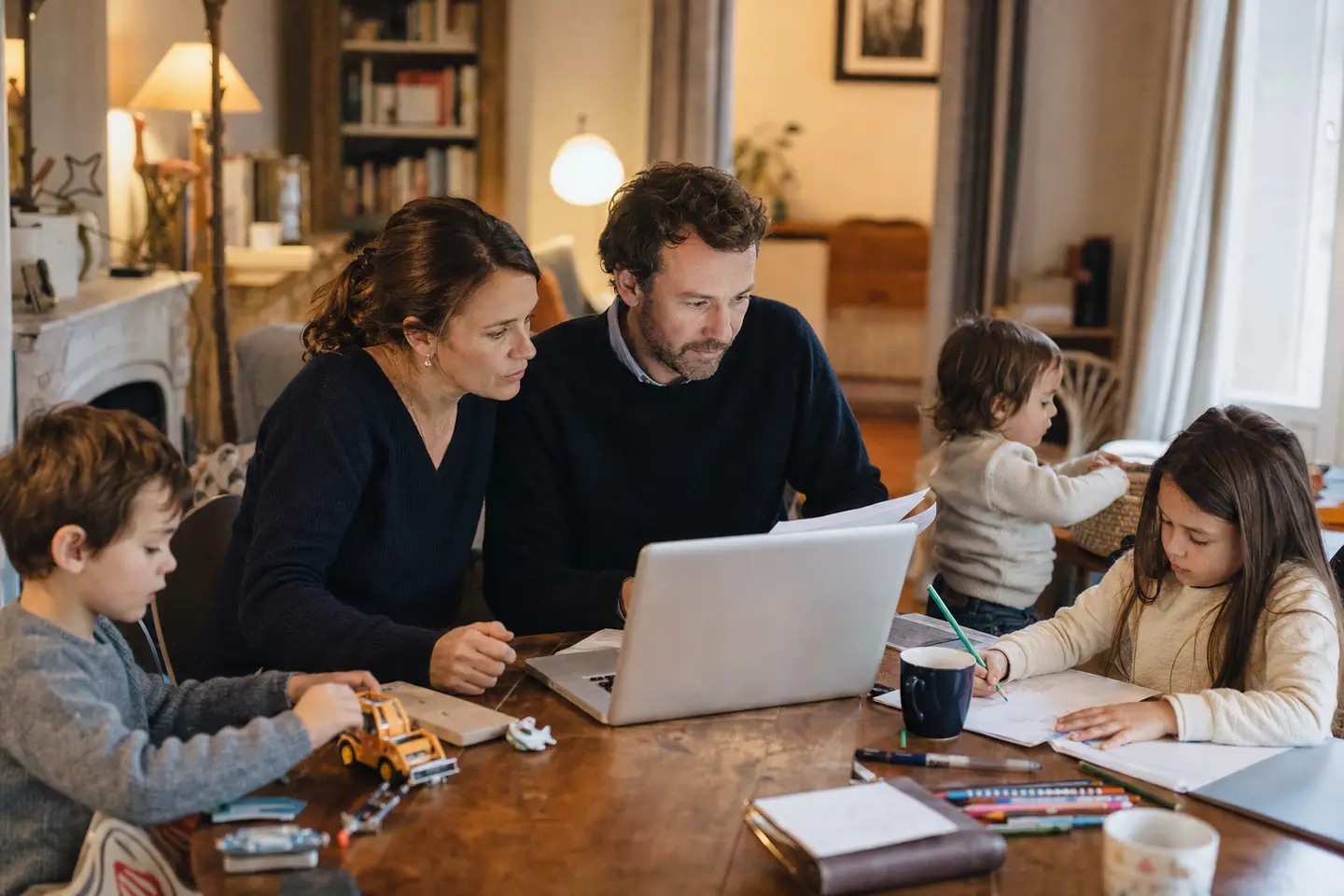 Parents comparant des offres de mutuelle famille sur un ordinateur portable pendant que leurs enfants jouent