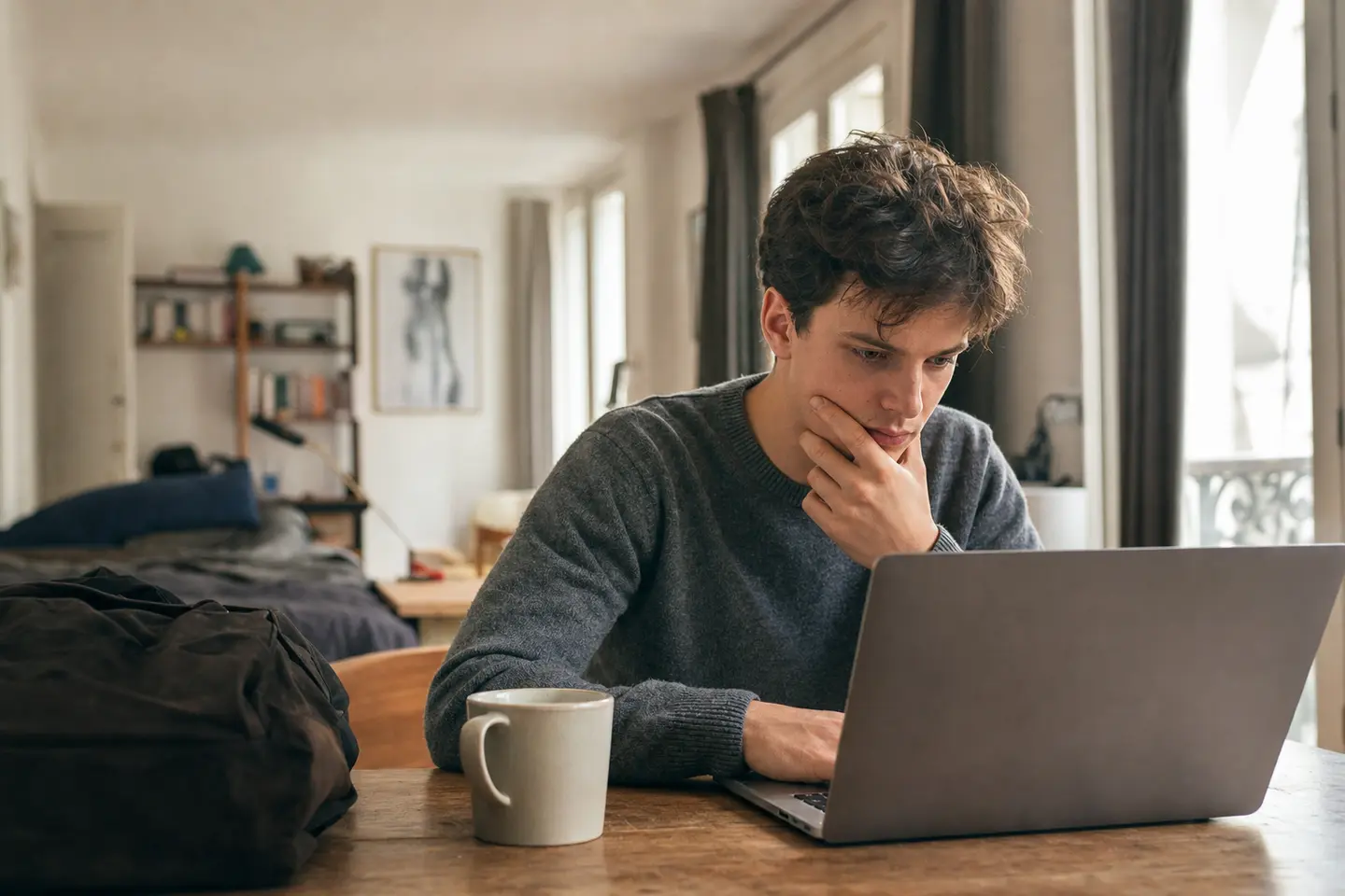 Un jeune actif compare des offres de mutuelle santé sur son ordinateur portable dans son studio, au début de sa vie professionnelle.