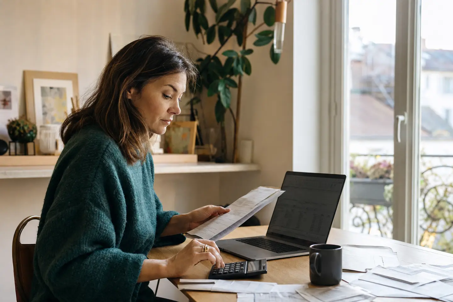 Travailleuse indépendante calculant son plafond de déduction Madelin avec une calculatrice et des relevés de cotisations dans son bureau