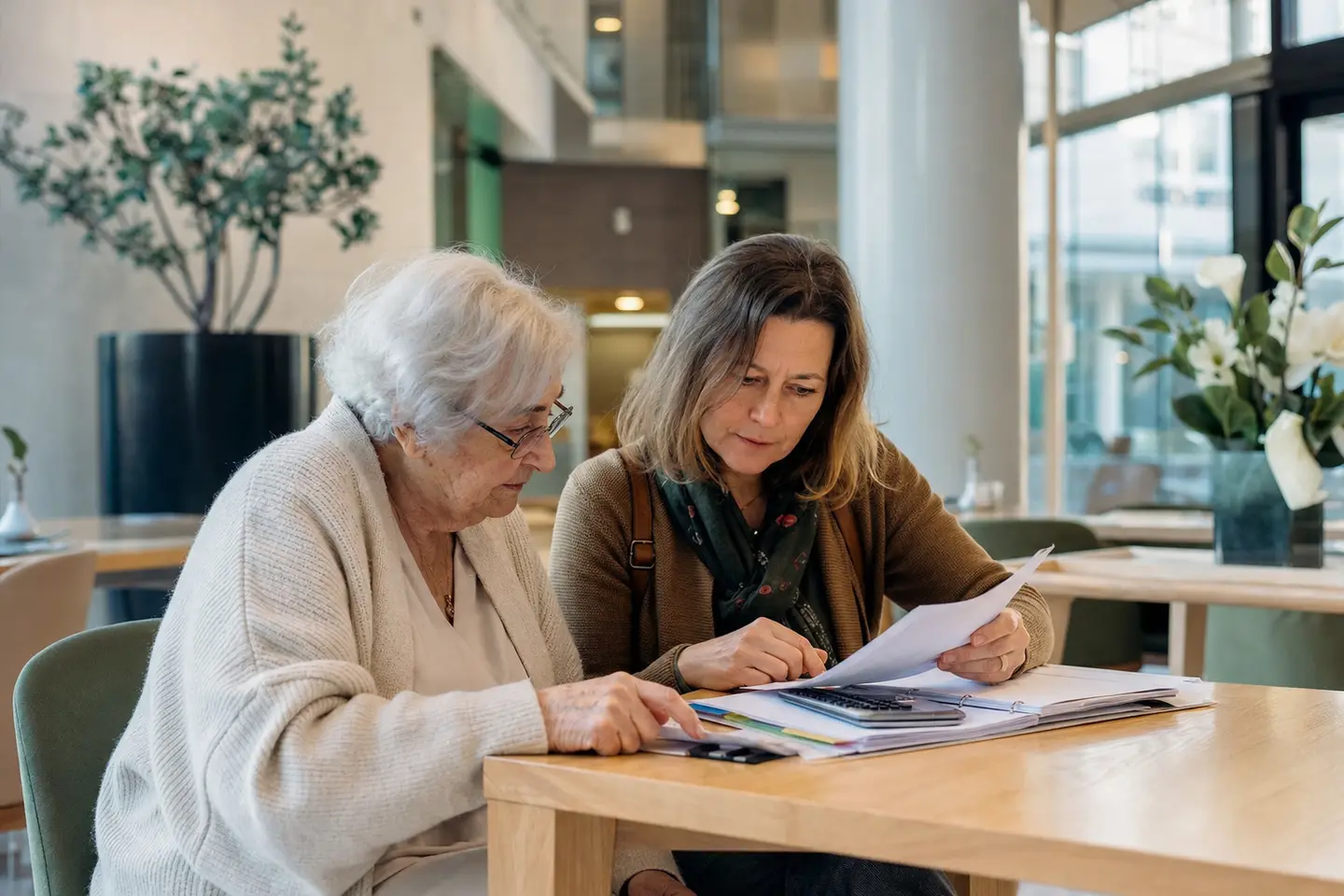 Une future résidente et sa fille comparent les devis d'hébergement dans le hall lumineux d'un EHPAD