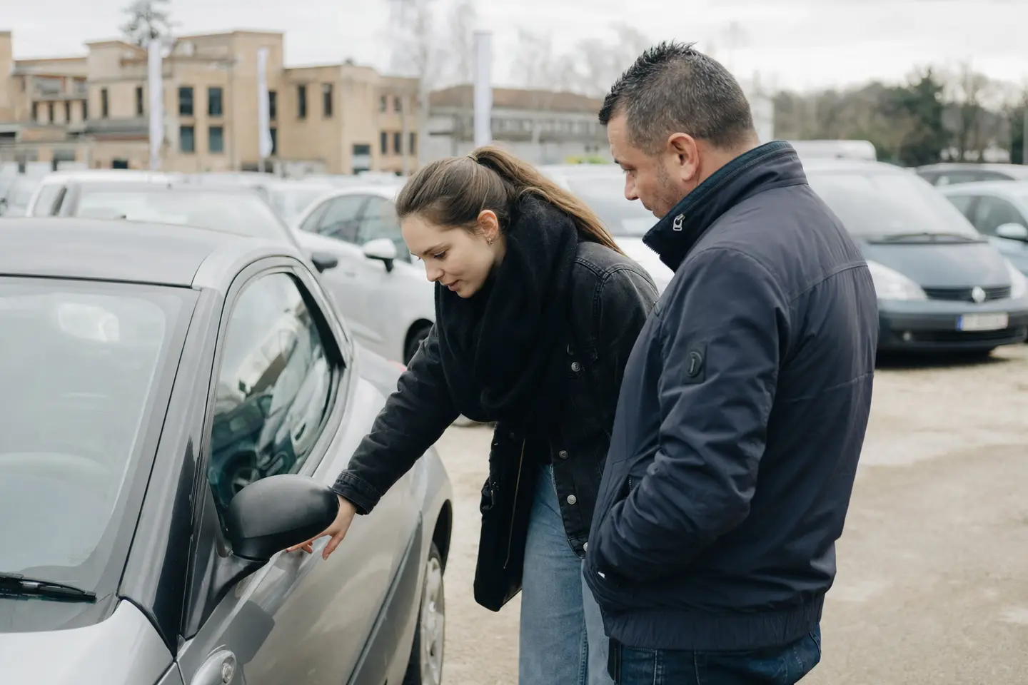 Une jeune conductrice examine une petite citadine d’occasion sur le parc d’un vendeur automobile